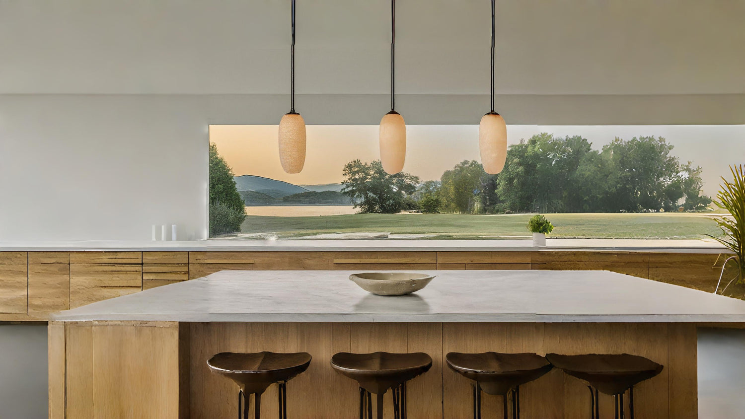 Modern pendant lights hang over a kitchen island with a view of a lake and mountains